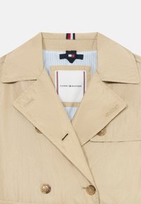 Beige dobbeltradet trenchcoat med en glat tekstur, der har store knapper, et broderet logo og et stribet blåt foret.