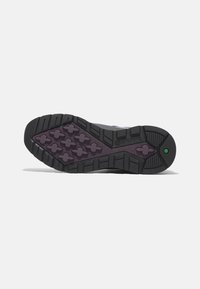 Suela de zapato de goma negra y morada con un diseño texturizado, que presenta agarraderas en forma de hexágonos y patrones en cruz para mayor tracción.