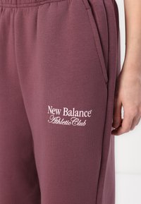 Bordo trenirke napravljene od mekog materijala imaju pojas sa vezicom i bočne džepove. "New Balance Athletic Club" je izvezen u beloj boji.