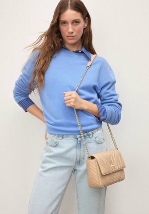 Pulover bleu deschis cu manșete drepte cu dungi, blugi din denim deschis și o geantă bej matlasată, purtată în diagonală, cu o închizătoare aurie și bretea cu lanț.