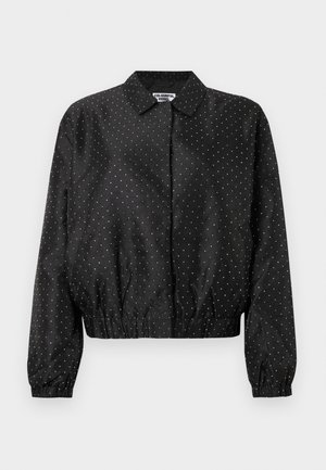 Casaco bomber preto com padrão de bolinhas brancas, com gola, bainha elástica e punhos franzidos. Textura do tecido lisa.