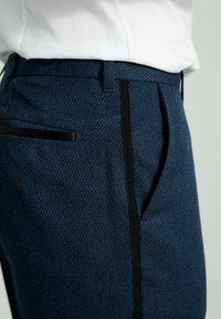 Marineblaue gemusterte Hosen mit strukturiertem Gewebe, ausgestattet mit schwarzen seitlichen Akzenten und einer Gesäßtasche. Maßgeschneiderte Passform mit Falten.