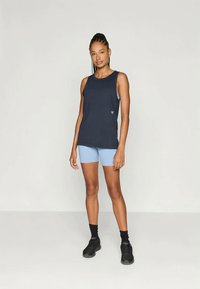 Navy sleeveless athletic top with a relaxed fit, paired with light blue bike shorts. Model wears black socks and sneakers. Simple design and functional.
