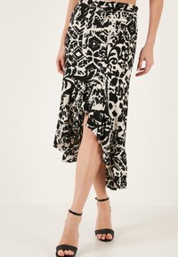 Jupe à motifs noir et blanc avec un ourlet volé, en tissu léger, présentant une fente jusqu'à la cuisse et une taille ajustée.
