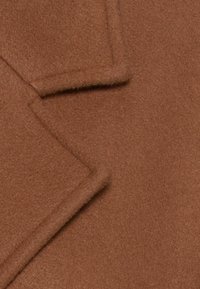 Brązowa tkanina wełniana na płaszcz o miękkim, teksturowanym wykończeniu z ukośnym detalem klapy. Gładki, ciepły wygląd bez widocznych wzorów.