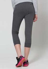 Leggings capri grises de algodón con un diseño ajustado, longitud recortada y puños enrollados, combinados con zapatillas negras con toques de color rosa.