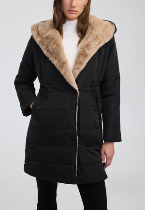 Zwarte donsjas met een beige nepbontkraag. Kenmerkt zich door een gewatteerd ontwerp, zijzakken en een verstelbaar trekkoord in de taille. Knopsluiting.