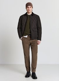 Giacca trapuntata marrone con colletto scuro, maglione verde oliva testurizzato, pantaloni beige di velluto a coste e stivaletti in pelle nera.