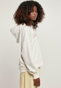Svetlosivý fleecový sweatshirt s prednou kapsou, kapucňou so šnúrkou a rebrovanými manžetami. Na prednej strane má ružový nápis a voľný strih.