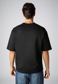 Schwarzes Baumwoll-T-Shirt mit Rundhalsausschnitt und kurzen Ärmeln, das einen lockeren Schnitt und eine glatte Textur aufweist. Die Rückansicht zeigt ein einfaches, klassisches Design.