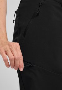 Zwarte stoffen broek met een gladde textuur, voorzien van een ritszak en verstelbare koorddetails in de taille.
