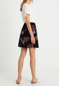 Černá květinová sukně s červenými a modrými květy, vrstvený design, zkombinovaná s bílým topem s krátkým rukávem a bílými nazouvacími botami.