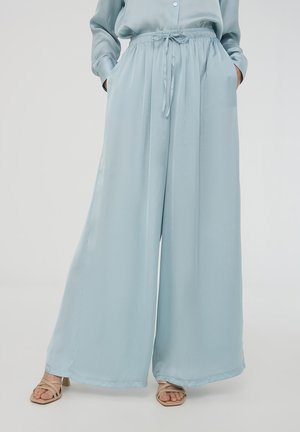 Pantaloni larghi blu chiaro realizzati in un tessuto morbido e fluido, con vita elastica e cordoncino regolabile, dotati di tasche laterali.