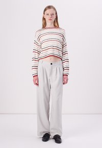 White cropped sweater with multicolored stripes, paired with wide-legged light gray trousers and black shoes. Simple design and relaxed fit.