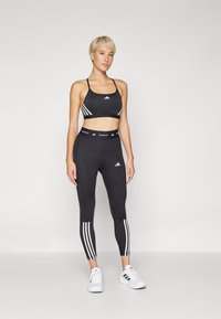 Zwart sportbeha en legging set gemaakt van rekbare, vochtregulerende stof. Kenmerkt zich door witte strepen aan de zijkanten en gebrandmerkte taillebanden.
