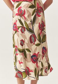 Jupe florale avec un fond crème, motifs botaniques rouge vif et vert, texture lisse et silhouette fluide. Les accents notables incluent des détails bleu foncé.