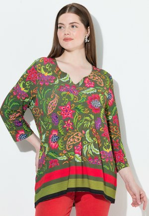 Groene tuniek met een levendig bloemmotief in roze, rood en blauw. Heeft een V-hals en driekwartmouwen, afgewerkt met horizontale strepen.