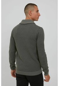 Suéter gris texturizado con un patrón de punto en diamante, un cuello ancho y puños acanalados. El diseño presenta una silueta ajustada y un color sólido.