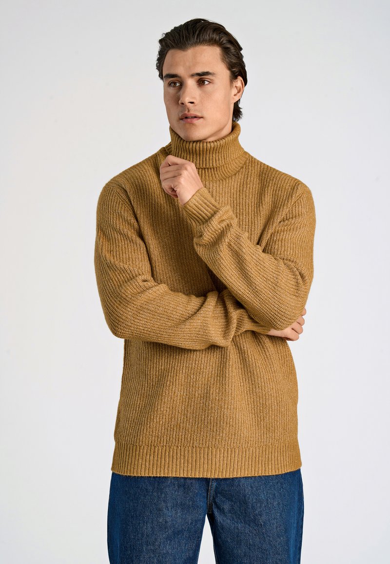 Senapsgul polotröja med ribbad struktur, långa ärmar och tjock fåll, kombinerad med mörkblå jeans.