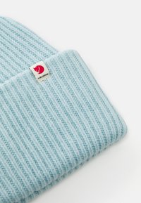 Light blue ribbed knit beanie with folded cuff and white tag featuring red fox logo and "Fjällräven" text.