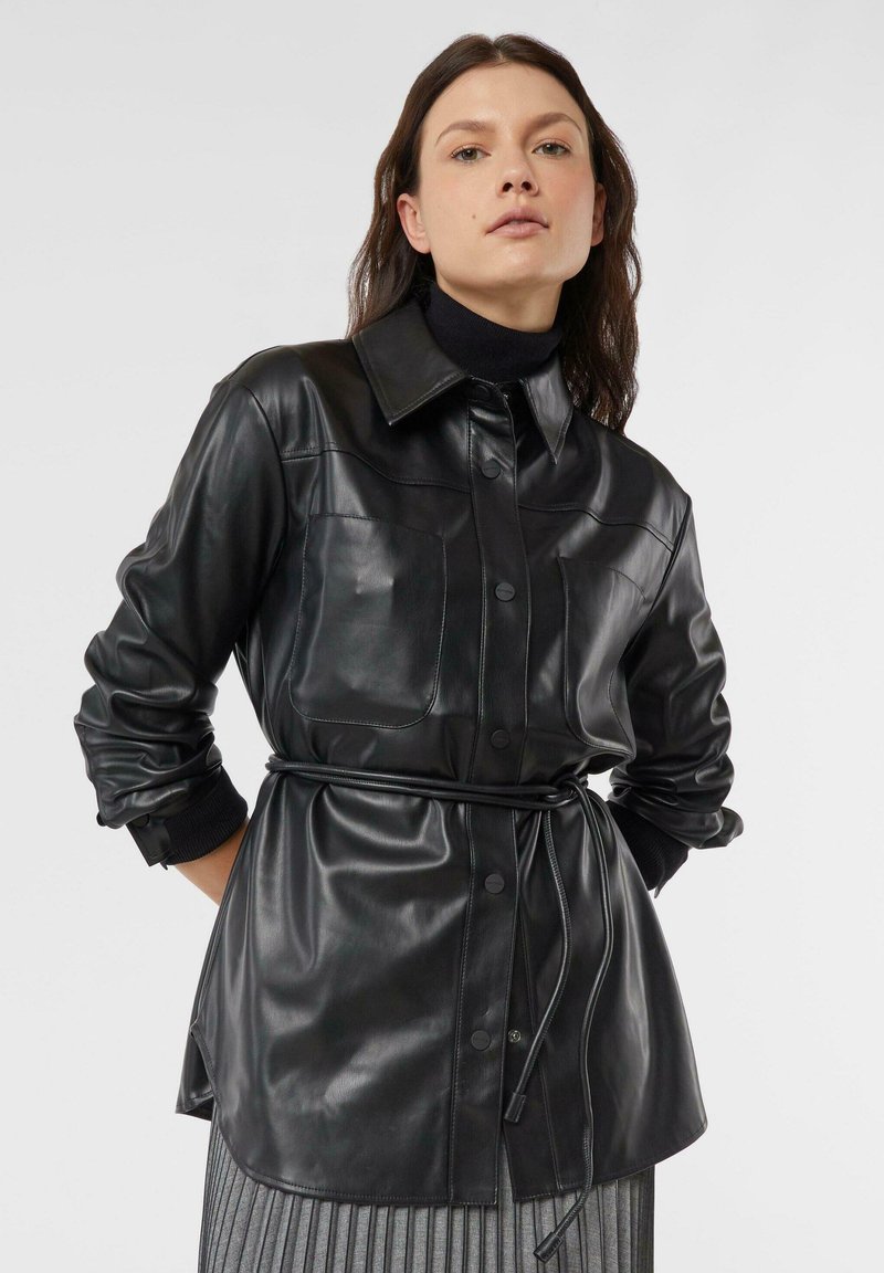 Czarna skórzana koszulowa kurtka z kołnierzykiem typu karo, przednimi kieszeniami, zapięciem na guziki oraz paskiem w talii. Gładka faktura z lekko błyszczącym wykończeniem.