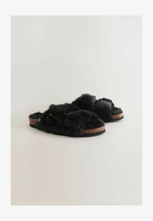 Schwarze, flauschige Hausschuhe mit Korksohle, die mit zwei auffälligen, flauschigen Riemen und dezenten goldenen Akzenten an den Riemen versehen sind. Weicher Stoff überall.