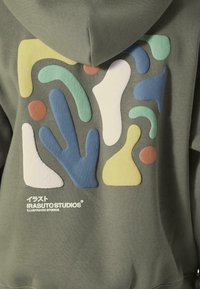 Hætte sweatshirt i olivengrøn med et struktureret, multifarvet abstrakt design på bagsiden. Har logo i hvidt nederst.