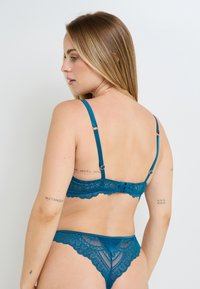 Bralette in pizzo verde petrolio e perizoma abbinato con bordi ondulati, spalline regolabili e dettagli con motivo floreale. Finitura in satin liscio.