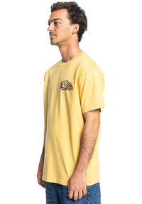 Geel katoenen t-shirt met korte mouwen, voorzien van een grafisch ontwerp in groen en rood op de linkerborst. Eenvoudige achterkant.