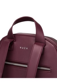 Burgundy faux leather backpack with a rounded shape; features a silver zipper and embossed logo; dual straps for carrying convenience.