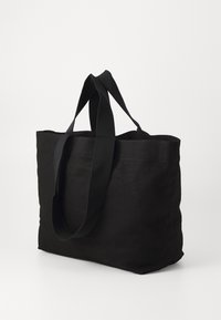 Borsa a tote in tela nera con manici larghi, forma rettangolare, fondo piatto e senza accessori visibili. Design semplice e resistente.
