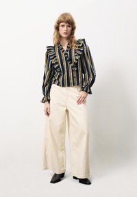 Blouse rayée avec des volants en marine et olive, associée à un pantalon large crème. Comprend des manches longues et une fermeture à boutons.