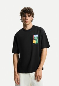 Black short-sleeve t-shirt featuring colored graphic text and a yellow circle design on the front. Made from a smooth, lightweight fabric.