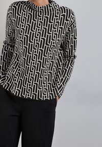 Pullover lavorato a maglia bianco e nero con un motivo geometrico, collo alto e maniche lunghe. La texture sembra morbida e leggermente strutturata.