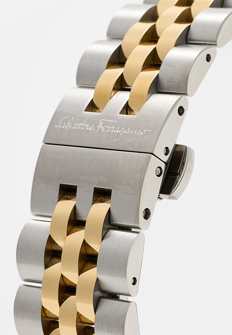 Bracelet de montre en métal avec des maillons en acier inoxydable poli et en or, avec une gravure de marque et un mécanisme de fermoir sécurisé.