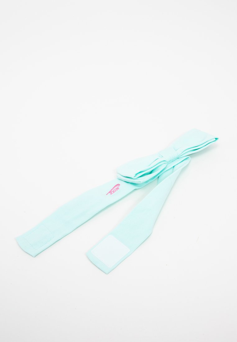 Un nœud en tissu vert menthe avec deux longues queues, mettant en avant une petite étiquette de logo rose et un patch rectangulaire blanc à une extrémité.