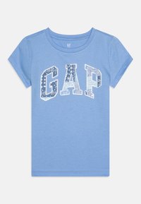 Gaiši zila kokvilnas t-krekls ar īsām piedurknēm un apaļu kakla izgriezumu, ar lielu balto "GAP" logotipu, kas rotāts ar ziedu motīviem.