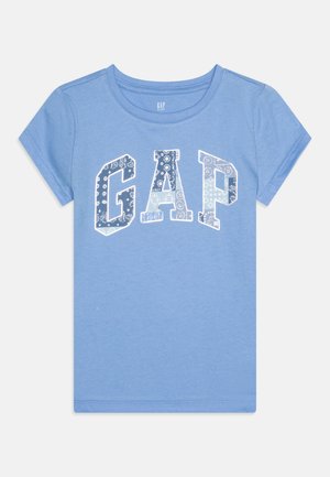 Gaiši zila kokvilnas t-krekls ar īsām piedurknēm un apaļu kakla izgriezumu, ar lielu balto "GAP" logotipu, kas rotāts ar ziedu motīviem.