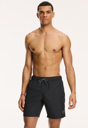 Schwarze Badeshorts mit elastischem Bund, Kordelzug und Logo-Patch. Das Material wirkt leicht und atmungsaktiv, geeignet für Wasseraktivitäten.