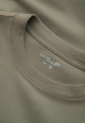 Olivgrön t-shirt med rund hals, som har en mjuk textur och tryckt etikett med varumärke och storleksinformation i vita bokstäver.