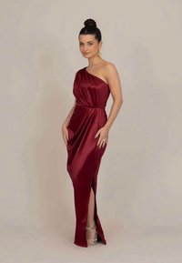 Satin burgundska obleka z enostranskim dizajnom, drapanimi detajli in razporkom do stegna. Poudarjena s srebrnimi sandali na trak.