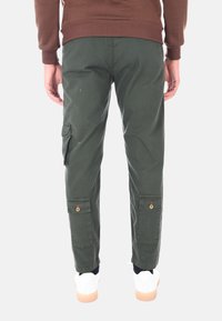 Pantaloni cargo verdi con tasche laterali, polsini elasticizzati e un bottone di accento rosso. Progettati con una vestibilità comoda e realizzati in tessuto di cotone resistente.
