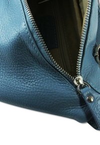 Blauwe leren handtas met een gestructureerd oppervlak, voorzien van een zilveren rits en een binnenvak in een lichtere stof, die een functioneel ontwerp toont.