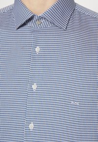 Kortärmad skjorta med knäppning, i ett blått och vitt rutmönster. Har en krage och två knappar på knäppningen. Subtil logotypdetalj.