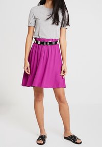 Lila kjol med elastisk midjeband och dekorativ silverdetalj, ihop med en grå t-shirt och svarta slidesandaler.