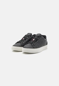 Sapatilhas de couro preto com um design texturizado, apresentando solas brancas, atacadores pretos e um destaque em vermelho e branco.