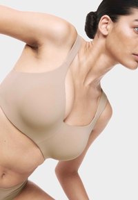 Top sportivo beige con texture liscia, spalline larghe e design arrotondato, caratterizzato da un scollo basso e bordi senza cuciture, adatto per abbigliamento attivo.