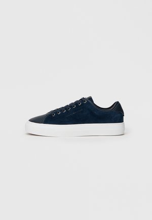 Marineblauer Wildleder-Sneaker mit glänzender, dunkler Zehenkappe, weißer Gummisohle und sechs Ösen für Schnürsenkel, mit einem dezenten Logo an der Seite.