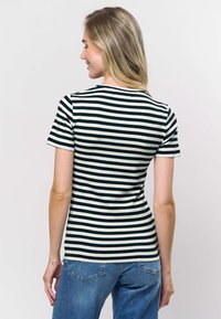 Musta-valkoraidallinen ribbattu t-paita, jossa on lyhyet hihat ja vartalonmyötäinen istuvuus, yhdistettysinisiin farkkuihin.