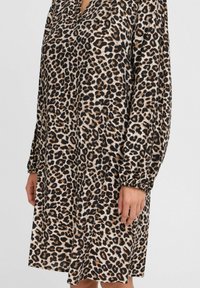 Leopardmönstrad klänning i svart, brunt och beige. Långa ärmar med samlade manschetter, avslappnad passform och V-halsdesign.
